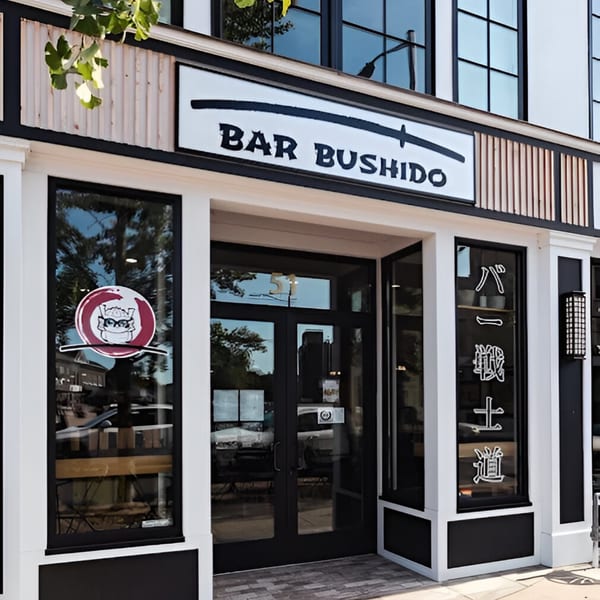 Exterior of Bar Bushido, a Japanese restaurant, with a black and white sign and glass doors.