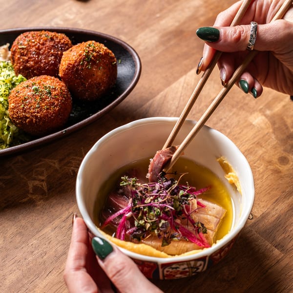 A person uses chopsticks to pick up a piece of fish from a bowl of Japanese food.