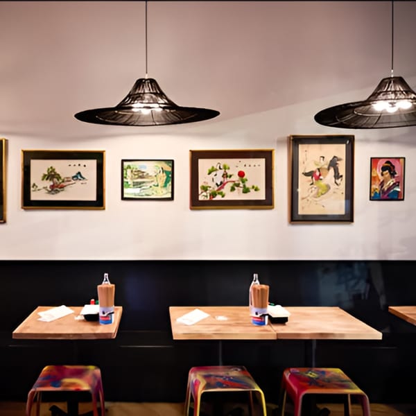 Japanese restaurant interior with framed art, wooden tables, colorful stools, and modern pendant lights.