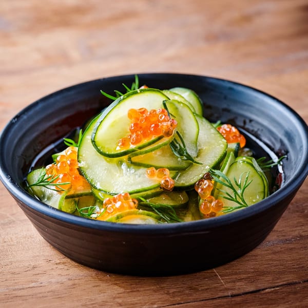Japanese cucumber salad with salmon roe and dill in a black bowl on a wooden table.