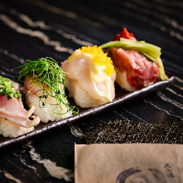 Four pieces of Bar Bushido's Japanese nigiri sushi with various toppings on a dark plate.