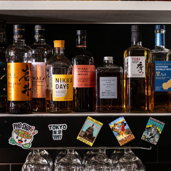 A shelf at Bar Bushido displaying various Japanese whisky bottles, with stickers below.