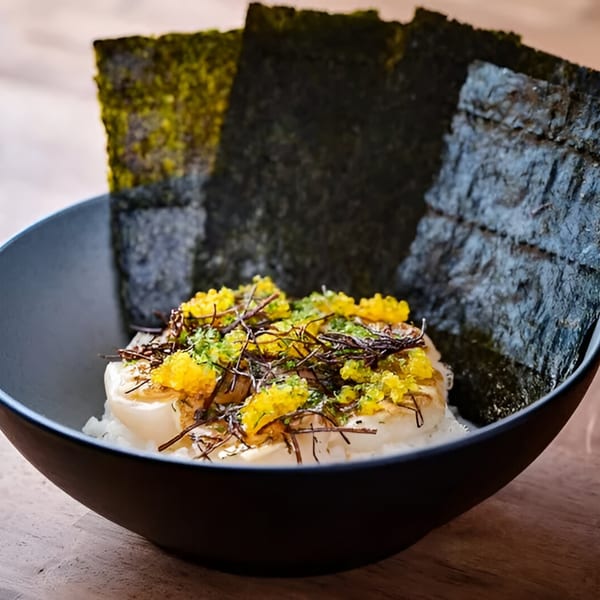 Japanese dish with scallops, yellow roe, and seaweed in a black bowl on a wooden table.